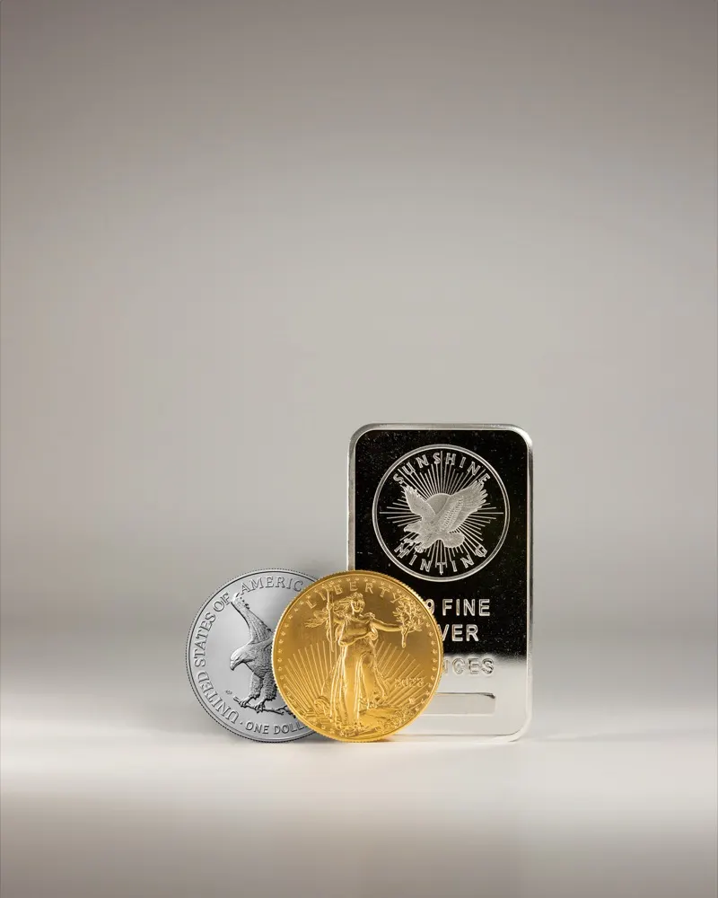 A gold coin and a silver coin standing in front of a silver bullion bar