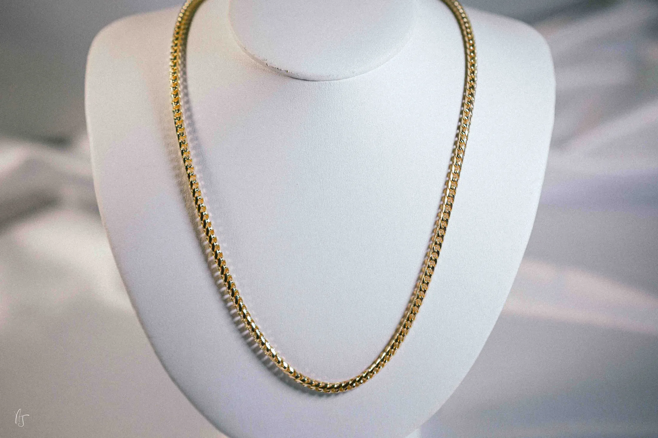 A gold curb link chain necklace on a white display bust