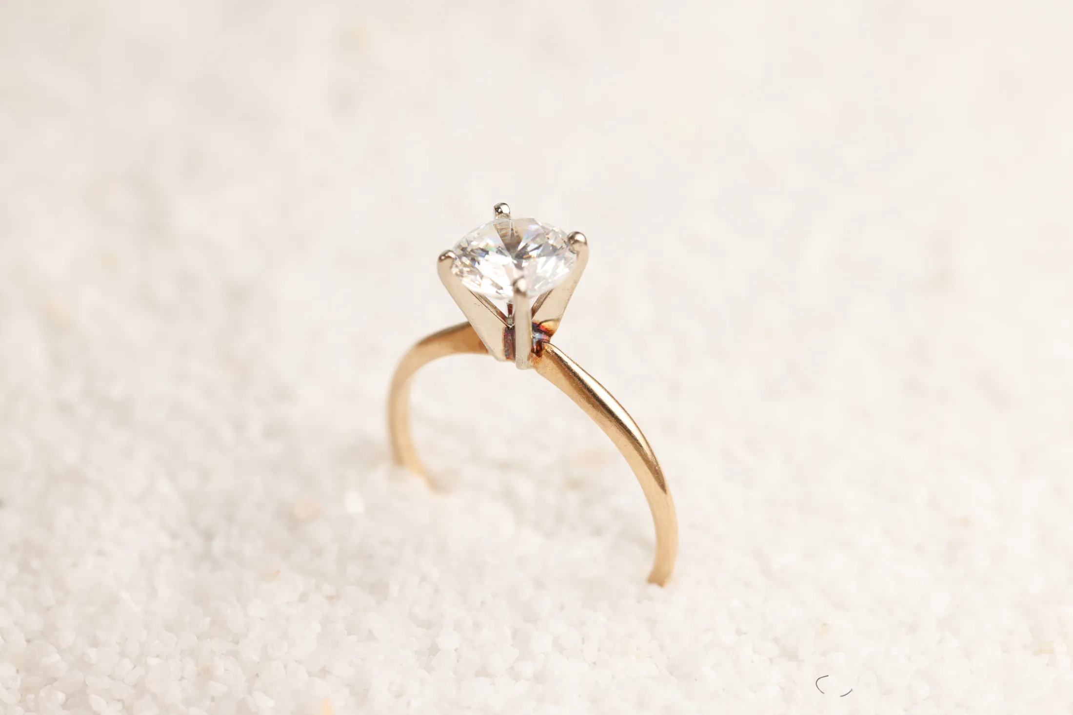 A gold solitaire engagement ring standing in white sand