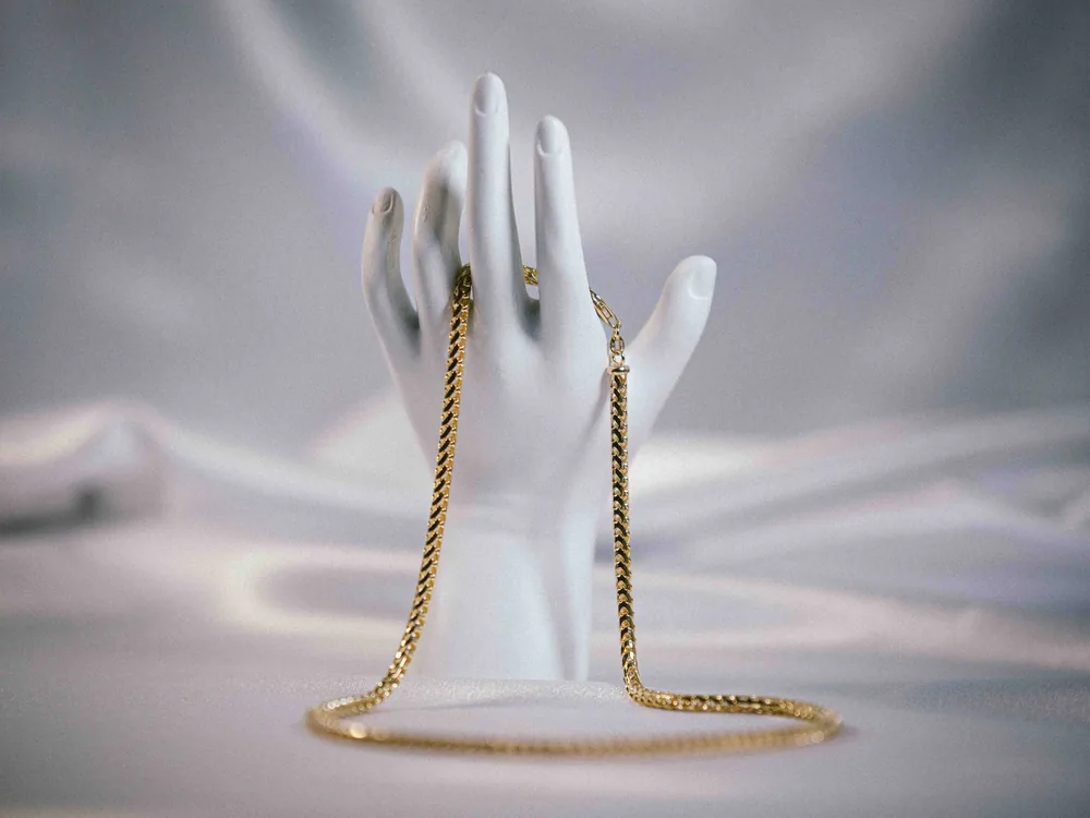A gold chain necklace draped over a white display hand