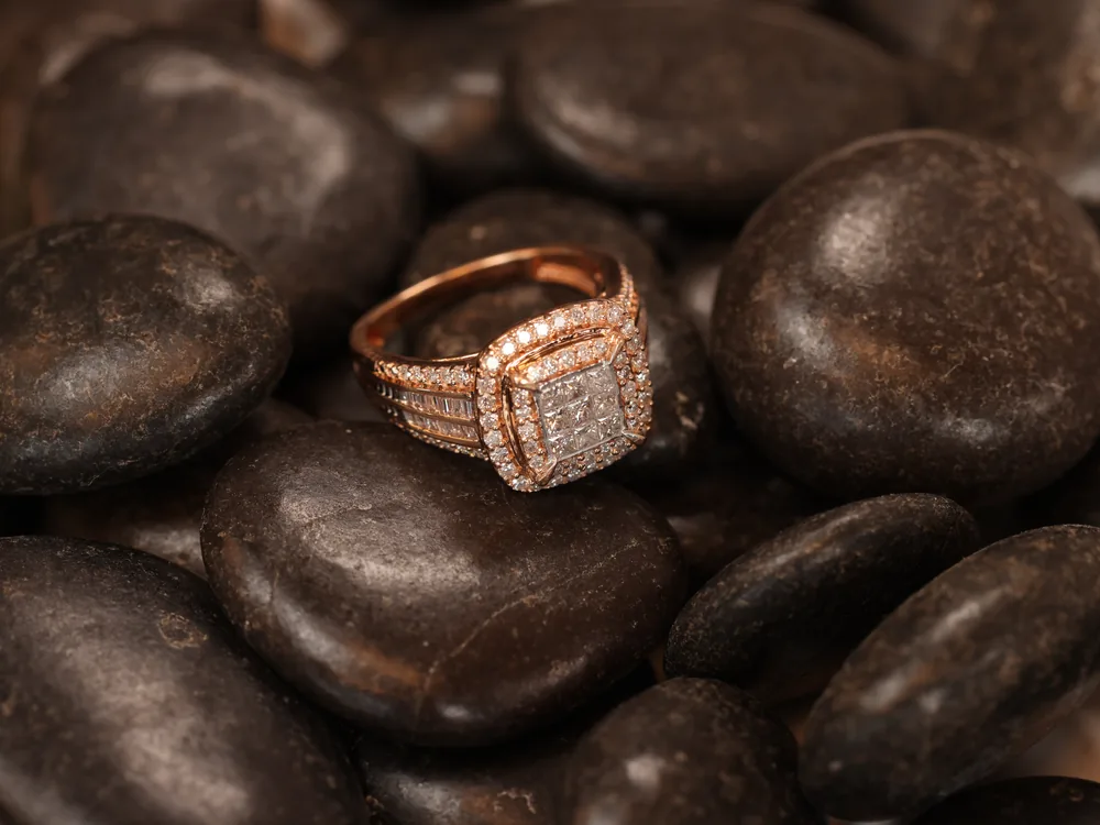 A rose gold diamond cluster ring resting on dark stones
