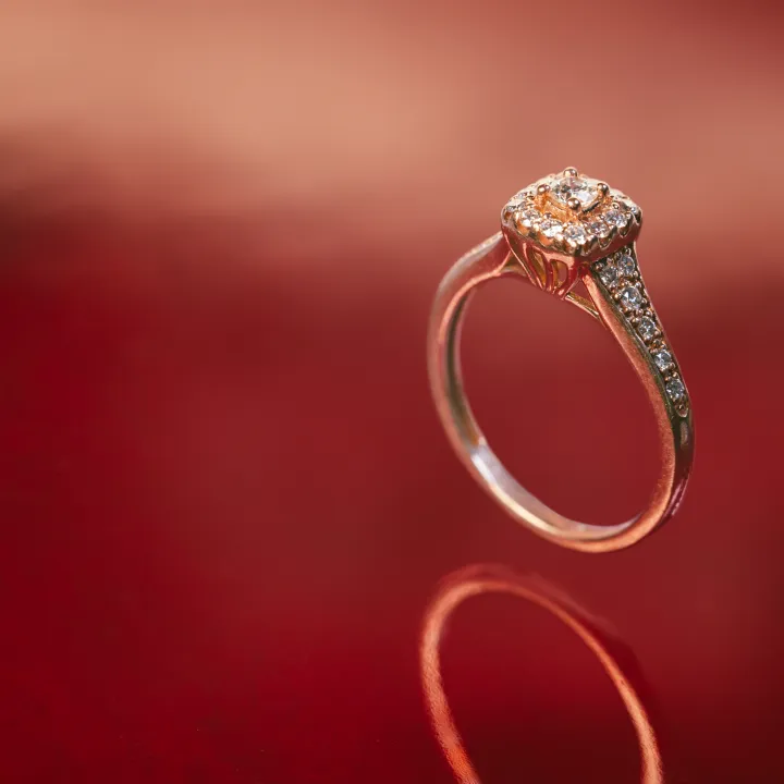 Diamond engagement ring with a round halo setting standing upright on a reflective red surface