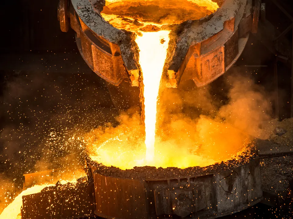 Molten metal pouring from a furnace ladle into a casting vessel amid sparks