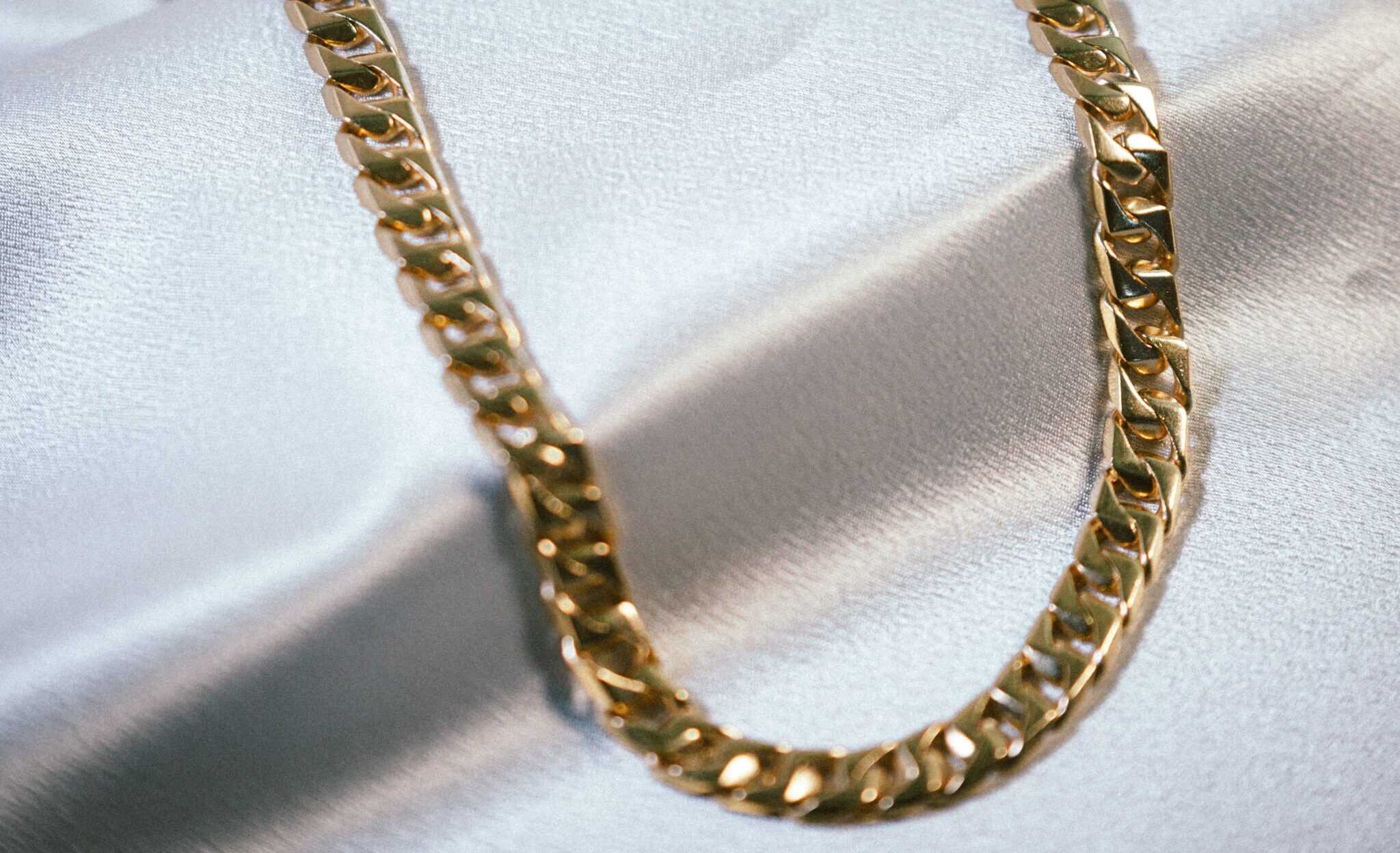 Close-up of a gold chain necklace on a satin background.