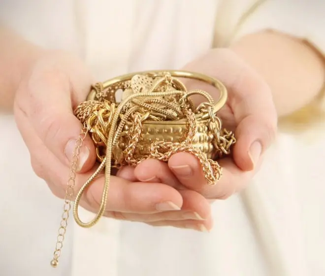Hand holding gold jewelry including necklaces and bracelets for precious metal investment.