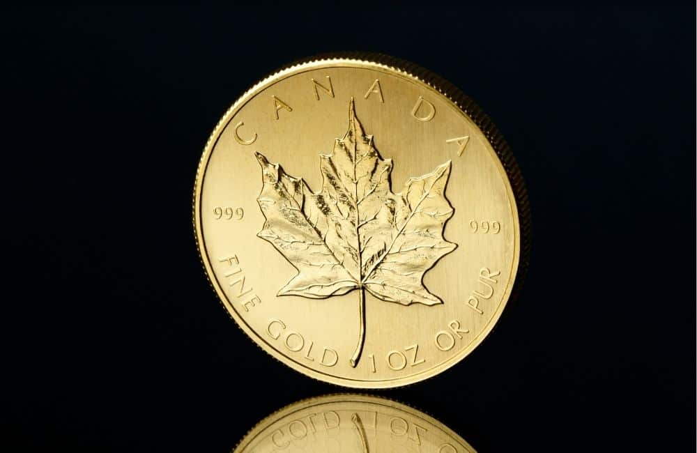 A gold canadian maple leaf coin on a reflective surface.