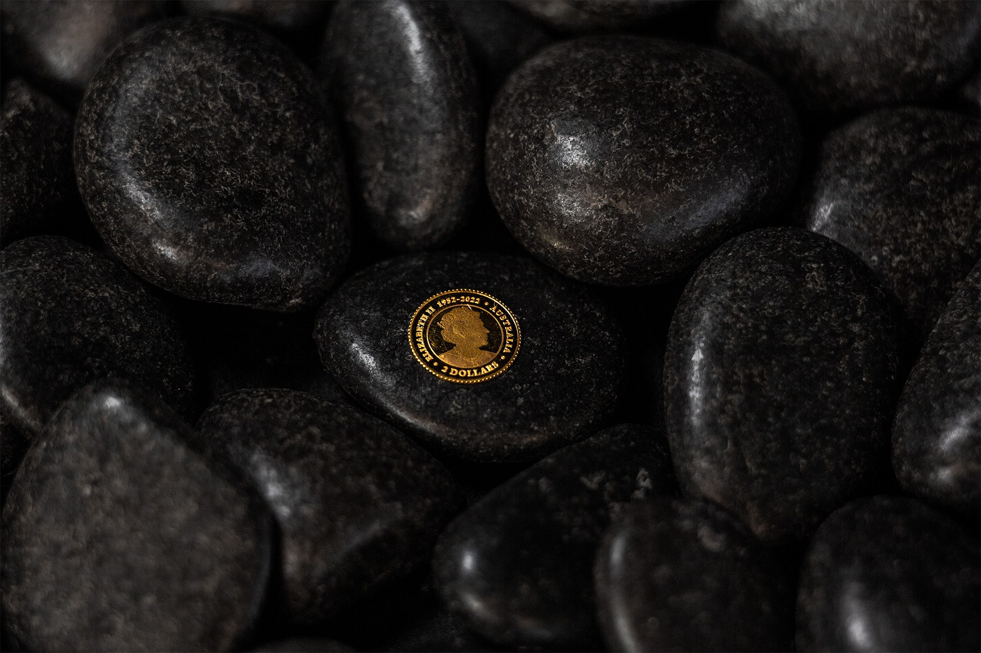 A 100 Gram CombiBar featuring a gold coin encircled by black pebbles.
